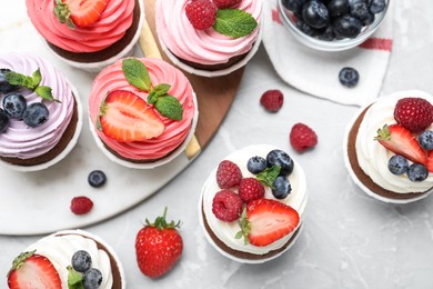 Sweet cupcakes with fresh berries on light marble table, flat lay.