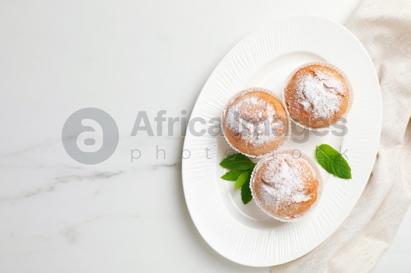 Photo of Tasty homemade muffins served with mint on white marble table, top view. Space for text