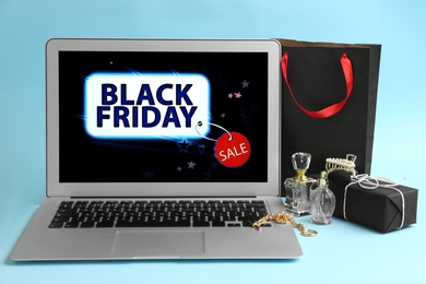 Laptop with Black Friday announcement, gifts and accessories on light blue background