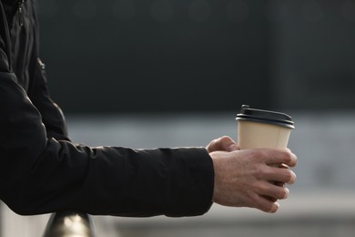 Photo of Man holding paper coffee cup outdoors, closeup