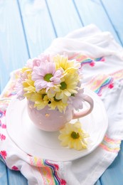 Bouquet of beautiful flowers in cup on light blue wooden table