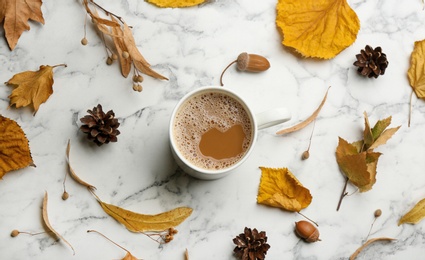 Flat lay composition with cup of hot drink and autumn leaves on white marble background. Cozy atmosphere