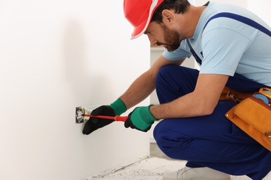 Photo of Electrician with screwdriver repairing power socket indoors
