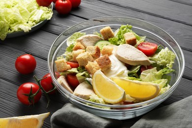 Bowl of delicious salad with Chinese cabbage, lemon, tomatoes and bread croutons on black wooden table