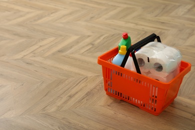 Shopping basket with household goods on wooden floor. Space for text