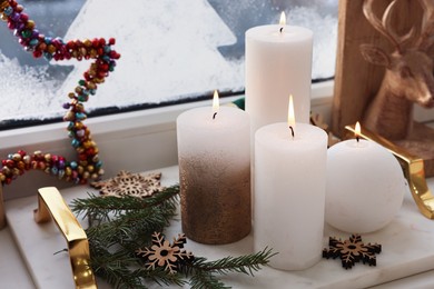 Beautiful burning candles with Christmas decor on windowsill indoors