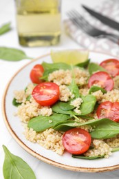 Photo of Delicious quinoa salad with tomatoes and spinach leaves served on white table, closeup