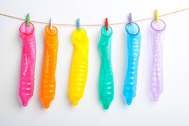Used colorful condoms hanging on clothesline against white background. Safe sex concept