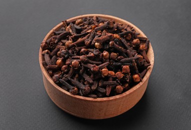 Aromatic dry cloves in wooden bowl on grey background, closeup