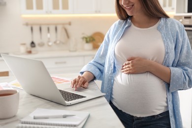 Pregnant woman working in kitchen at home, closeup. Maternity leave