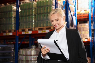 Happy manager holding clipboard in warehouse with lots of products. Space for text