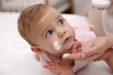 Photo of Mother applying moisturizing cream on her little baby at home, closeup