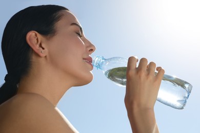 Beautiful young sportswoman drinking water outdoors, closeup. Refreshing drink