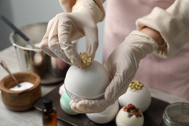 Woman in gloves decorating bath bomb with flower at table, closeup