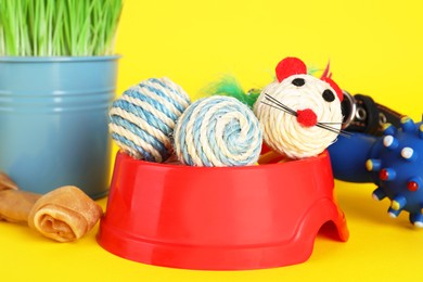 Various pet toys, bowl and wheatgrass on yellow background, closeup