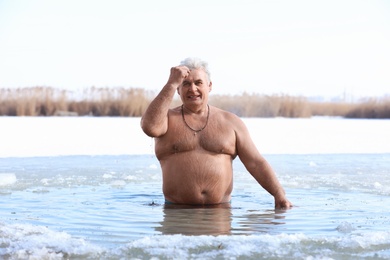 Mature man immersing in river on winter day. Baptism ritual