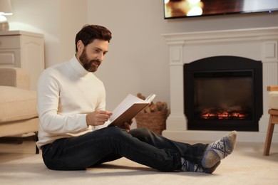 Photo of Handsome man reading book near fireplace in room