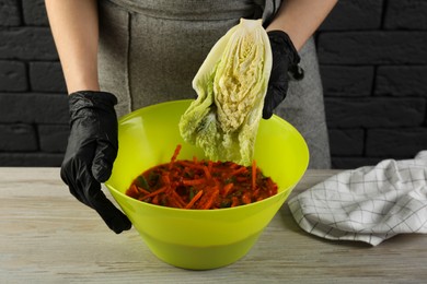 Woman preparing spicy cabbage kimchi at wooden table indoors, closeup