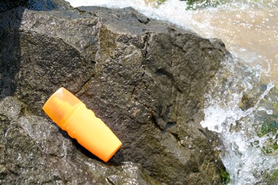 Photo of Bottle with sun protection spray on rock near sea tide, space for text