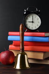 Golden school bell, apple, alarm clock and books on wooden table near blackboard