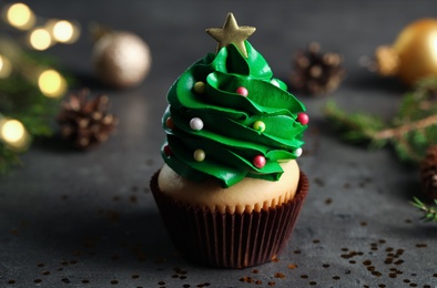 Cupcake decorated with creamy Christmas tree on dark table, closeup