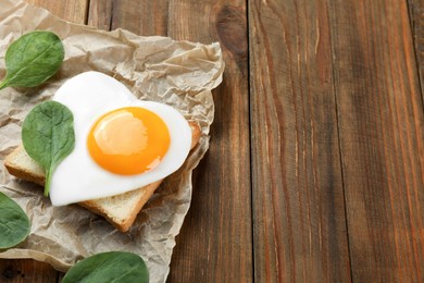 Photo of Tasty toast with heart shaped fried egg and spinach on wooden table, space for text