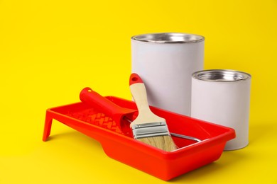 Photo of Cans of orange paint, brush, roller and container on yellow background