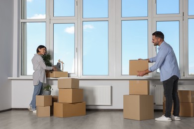 Photo of Happy couple with moving boxes near big window in new apartment