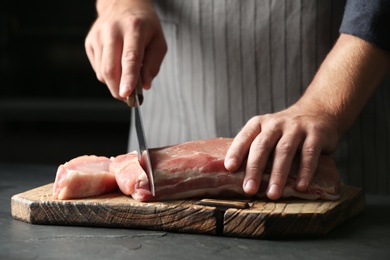 Photo of Man cutting fresh raw meat on grey table, closeup