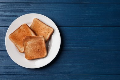 Photo of Plate with slices of delicious toasted bread on blue wooden table, top view. Space for text