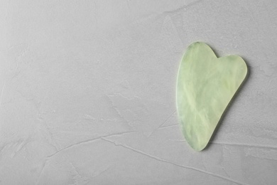 Photo of Jade gua sha tool on grey table, top view. Space for text
