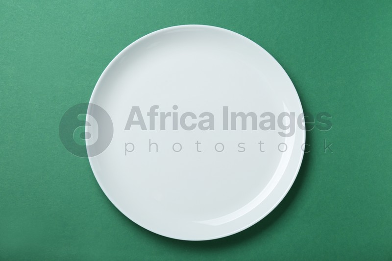Empty white ceramic plate on green background, top view