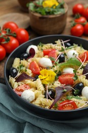 Bowl of delicious pasta with tomatoes, olives and mozzarella on wooden table, closeup