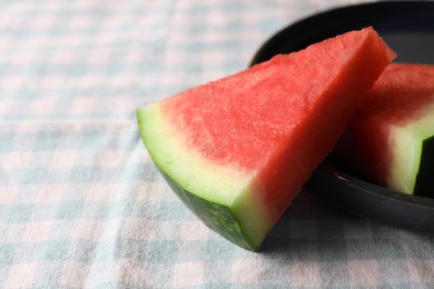 Sliced fresh juicy watermelon on checkered light blue tablecloth, closeup