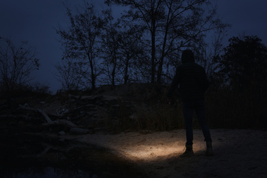 Man with flashlight walking near river in evening