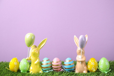 Easter bunny figures and dyed eggs on green grass against violet background