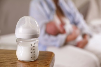 Photo of Mother and her little baby at home, focus on bottle of milk. Space for text