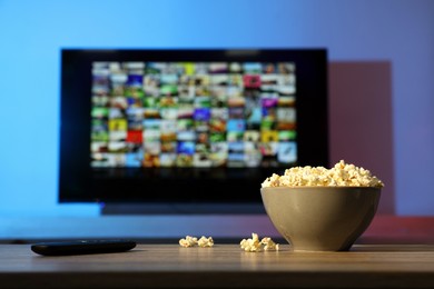 Photo of Bowl of popcorn and TV remote control on table indoors. Space for text