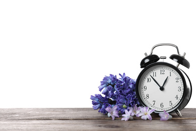 Black alarm clock and spring flowers on wooden table against white background, space for text. Time change