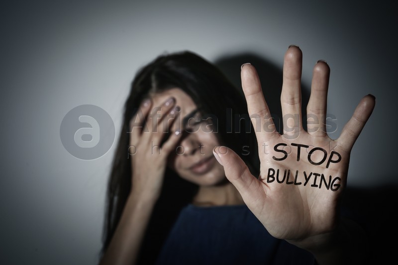 Crying teen girl showing palm with message STOP BULLYING near white wall, focus on hand