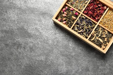 Different dry herbal teas in wooden box on grey table, top view. Space for text