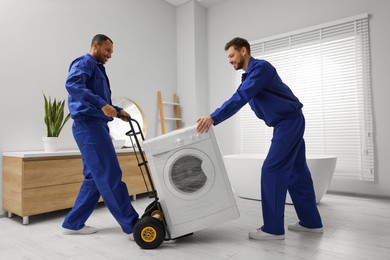 Photo of Male movers carrying washing machine in bathroom. New house