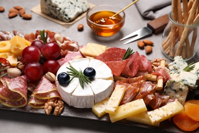 Wooden board with different appetizers on grey table, closeup