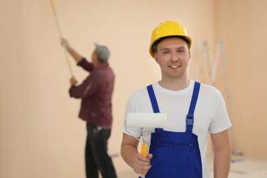 Photo of Worker holding paint roller in unfinished room. Painting walls