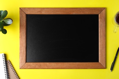 Clean small chalkboard, plant and stationery on yellow background, flat lay