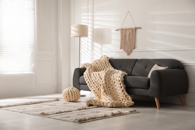 Photo of Soft chunky knit blanket on sofa in living room. Interior design
