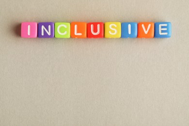 Photo of Colorful cubes with word Inclusive on beige background, flat lay. Space for text