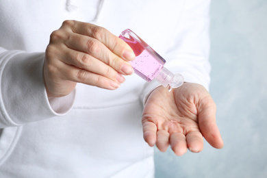 Photo of Woman applying antiseptic gel on hand against light background, closeup