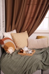 Comfortable lounge area with knitted blanket and soft pillows near window in room