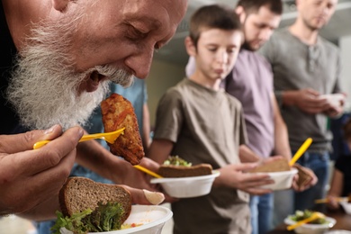 Senior man with other poor people eating food in charity centre
